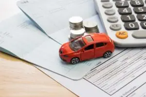 miniature car on insurance paperwork next to coins