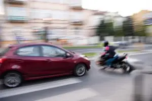 A motorcycle swerving in front of a red car.