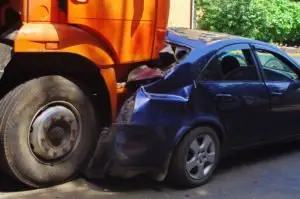 An orange truck crushing the truck of a blue car.