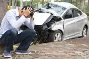 An upset man crouched near his damaged silver car.