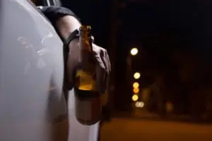 man holding open container of alcohol while driving