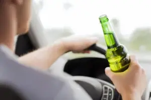 man holding beer bottle behind the wheel