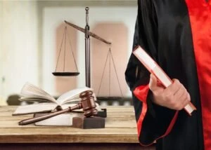 A lawyer in a black robe holds a book with a red cover.