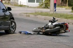 damaged motorcycle lying on the road next to a black car with fender damage