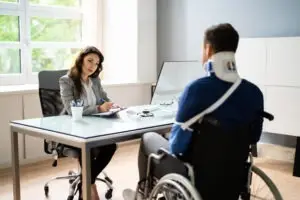 A man in a wheelchair with his arm in a sling and wearing a neck brace speaking with an experienced drunk driving accident lawyer in Rancho Cordova.