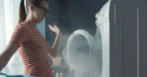 A woman standing inn from of an open washing machine with smoke pouring out.