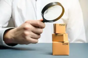 A product liability lawyer holds a magnifying glass over boxes with defective products.