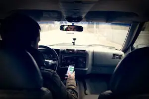 A view from the rear seat of a vehicle of a driver texting on his phone.