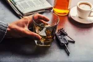 A close-up of a hand holding a whiskey glass next to a set of car keys.