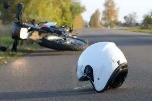 A wrecked motorcycle with a white helmet on the road in the foreground.