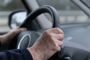 Older person driving car with hands on wheel.