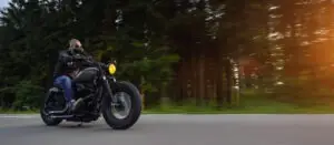 Man rides a motorcycle through a forest area without a helmet.