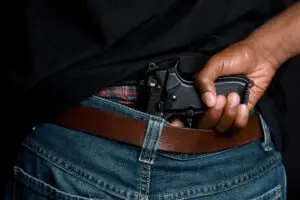 A man wearing a black shirt has his hand on a gun in the waist of his jeans.