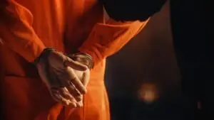A man is wearing an orange jumpsuit and is handcuffed.