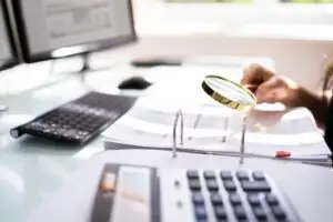 An insurance fraud lawyer uses a magnifying glass to examine evidence.