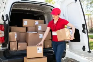 delivery truck driver in red attire holds and unloads boxes from truck