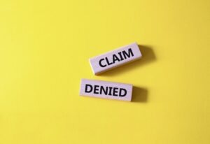 Two wooden blocks with “claim” and “denied” written on them on a yellow background.