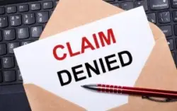 An overhead view of a brown envelope on top of a laptop keyboard with a white card with a red “claim denied” stamp.