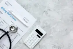 An overhead view of a billing statement, a stethoscope, and a calculator.