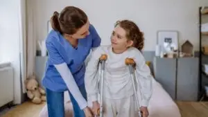nurse helping little girl on crutches
