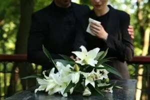 people grieving at a tombstone covered in white lilies