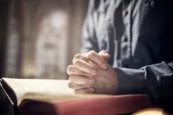 priest hands folded on a bible