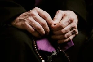 a priest holding rosary beads. Insights into the LA Catholic Church’s $880M sexual abuse settlement.