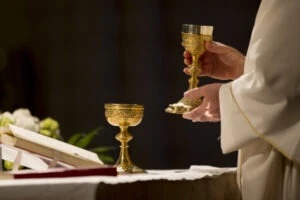 A priest holding a cup. How to report clergy abuse at the diocese of Grand Rapids.