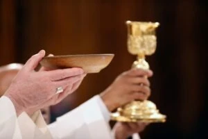 A priest holding up a communion plate. How to report clergy abuse at the Diocese of Lansig.