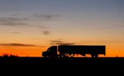 Silhouette,of,a,large,truck,driving,on,a,road,at