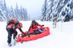 Two ski patrol workers leaning over an injured skier in a red rescue sled