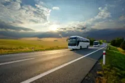 Two,white,buses,traveling,on,the,asphalt,road,in,rural